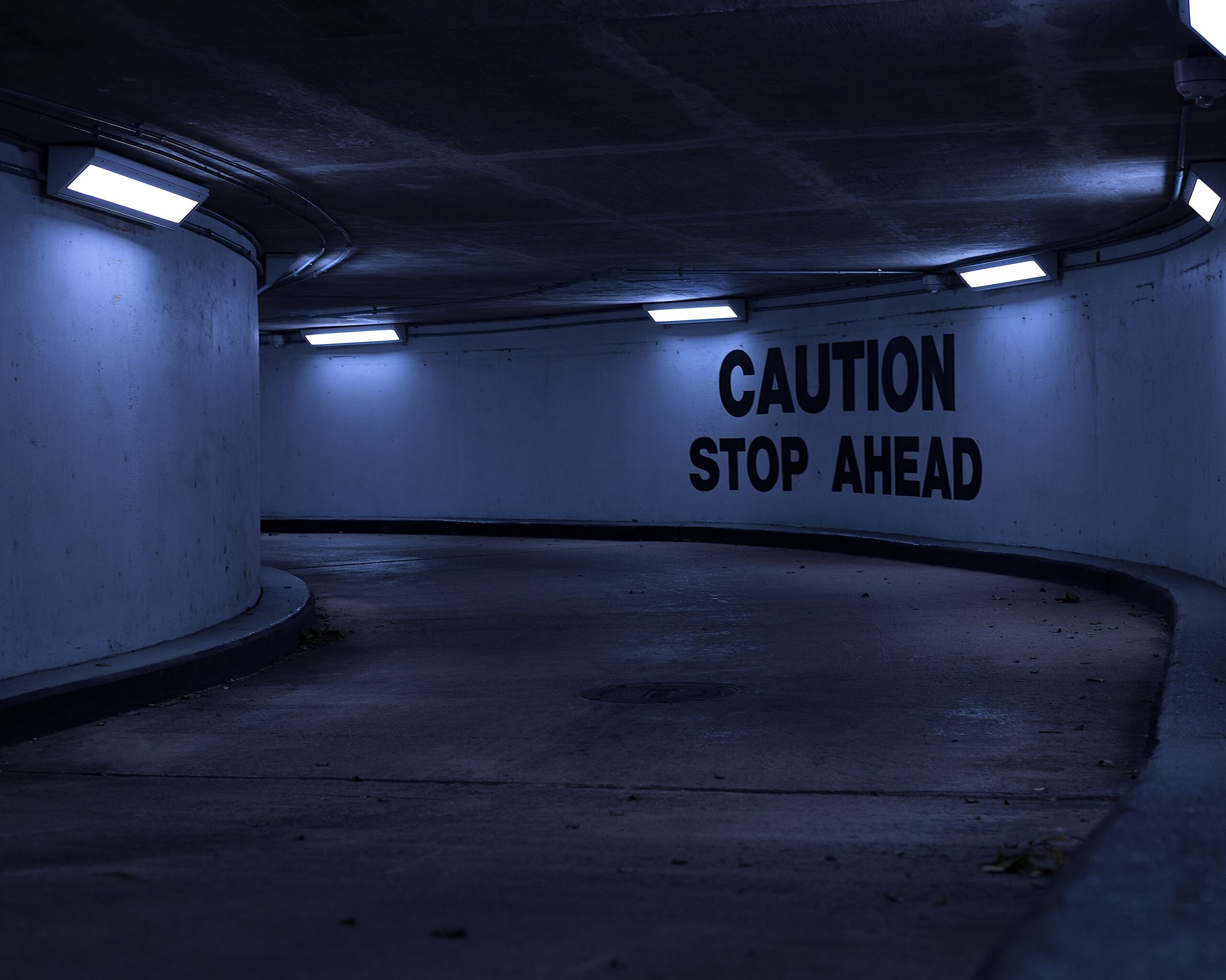 A picture of a dark narrowing road with the words "Caution: Stop Ahead" on the wall. This image was used to visualize the importance of proceeding with caution when working with AI and other related technology.